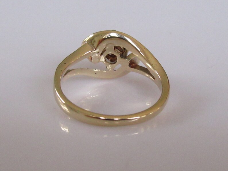 May include: A gold ring with a single round diamond in the center and two smaller diamonds on either side. The ring is set in a twisted band.