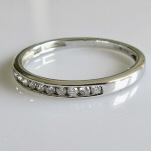 May include: A silver band with a row of small diamonds set in a channel setting.