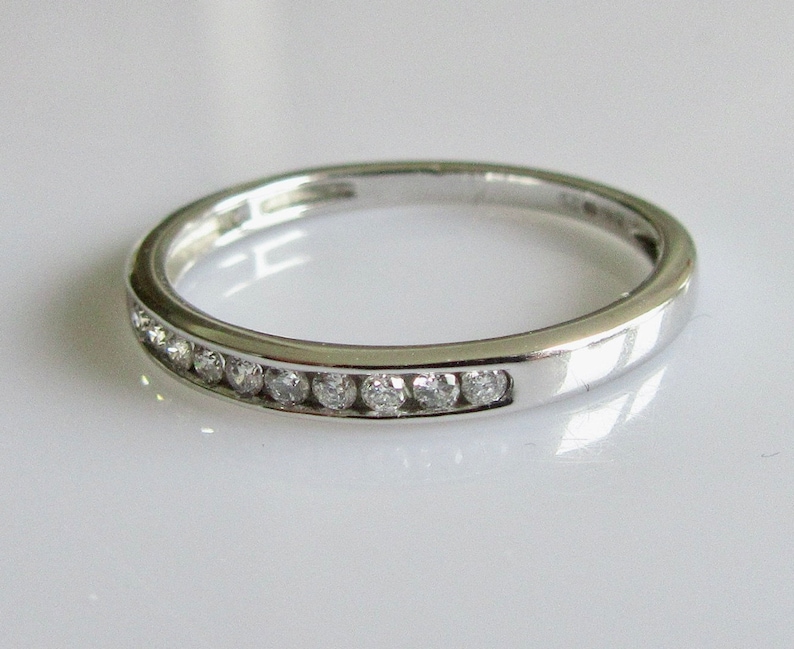 May include: A silver band with a row of small diamonds set in a channel setting.