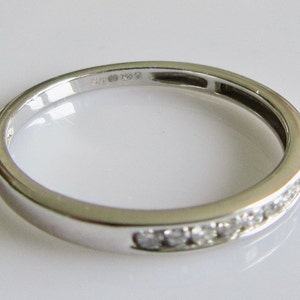 May include: A thin silver band with a row of small diamonds set into the metal. The band is marked "585 750".