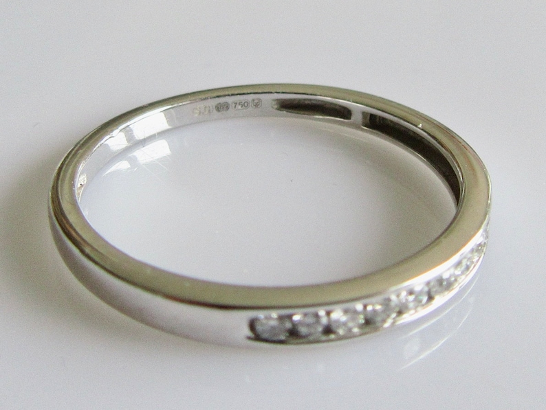 May include: A thin silver band with a row of small diamonds set into the metal. The band is marked "585 750".
