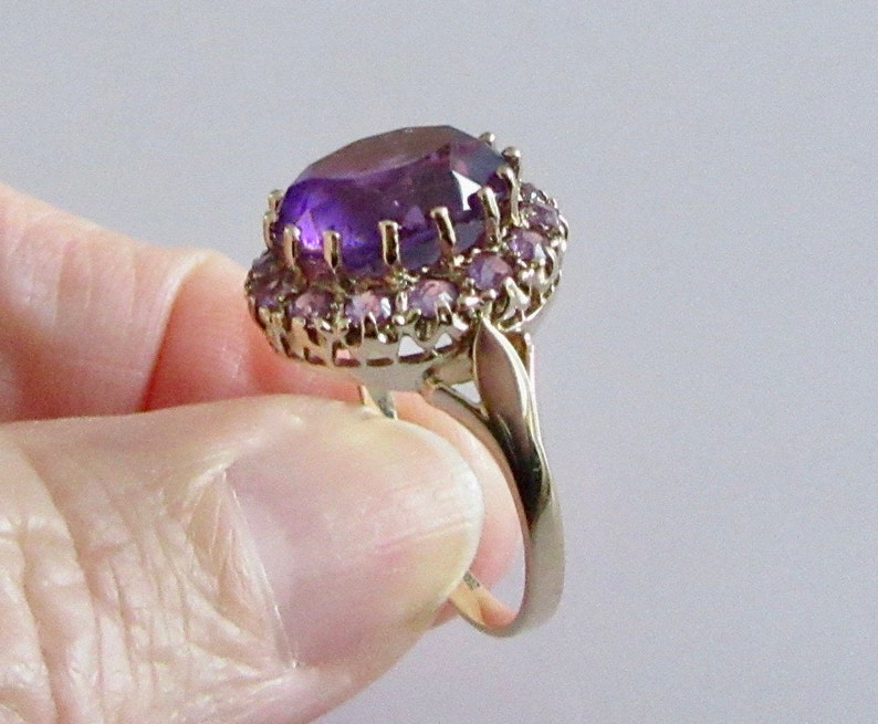 May include: A gold ring with a large, oval-shaped amethyst gemstone surrounded by a halo of smaller amethyst stones.