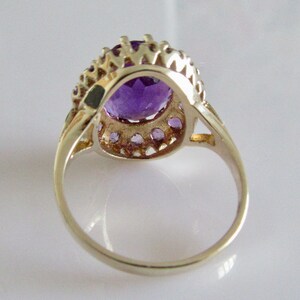 May include: A silver ring with a large oval amethyst gemstone surrounded by a halo of smaller amethyst stones.