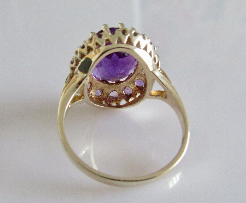 May include: A silver ring with a large oval amethyst gemstone surrounded by a halo of smaller amethyst stones.