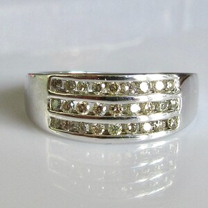 May include: A silver band ring with three rows of small, clear diamonds.