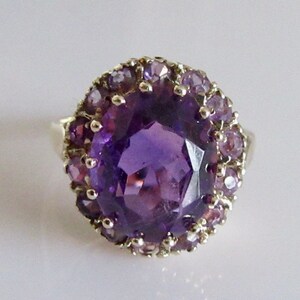 May include: A purple amethyst ring with a large center stone surrounded by smaller amethyst stones.
