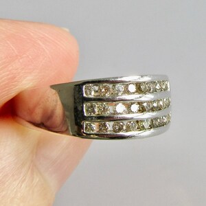May include: A silver band ring with three rows of small, clear diamonds.