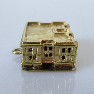 Puede incluir: Encanto de oro en forma de edificio con una fachada detallada y ventanas. El encanto tiene un bucle para sujetarlo a un collar o pulsera.