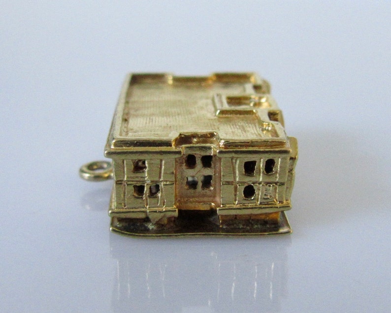 Puede incluir: Encanto de oro en forma de edificio con una fachada detallada y ventanas. El encanto tiene un bucle para sujetarlo a un collar o pulsera.