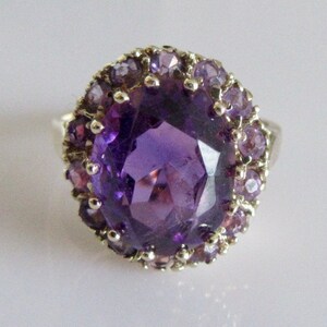 May include: A silver ring with a large, oval-shaped amethyst gemstone surrounded by a halo of smaller amethyst stones.