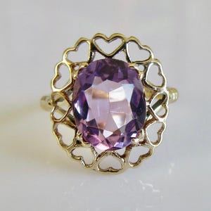 May include: A gold ring featuring a heart-shaped design and a large, oval amethyst gemstone.