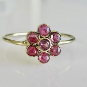 以下が含まれることがあります： ピンクの宝石で花のデザインが施された金の指輪です。