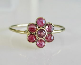 Puede incluir: Un anillo de oro con un diseño de flor hecho de piedras preciosas rosas.