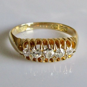 May include: A gold band ring with five round diamonds set in a delicate, openwork design. The ring is marked "9ct" on the inside.