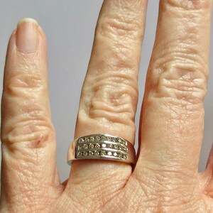May include: A silver band ring with three rows of small, clear diamonds.