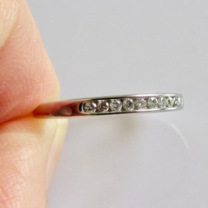 May include: A silver band ring with a row of small, clear diamonds set in a channel setting.