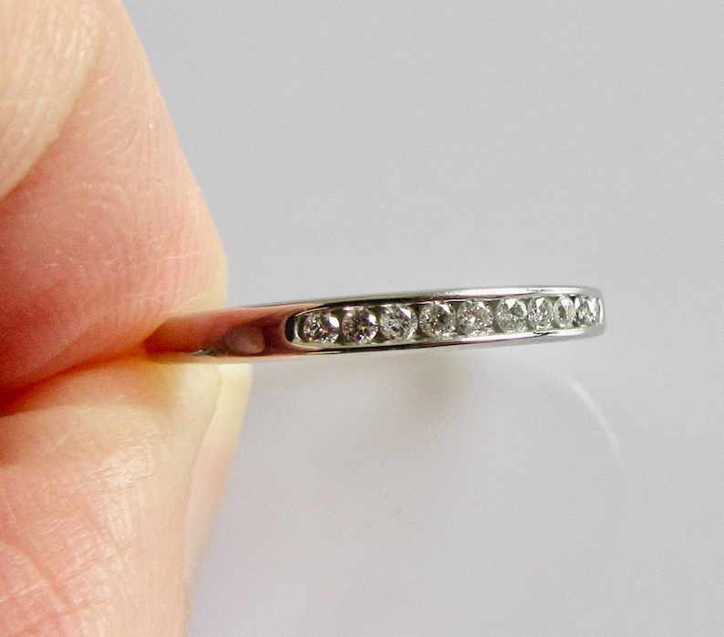 May include: A silver band ring with a row of small, clear diamonds set in a channel setting.