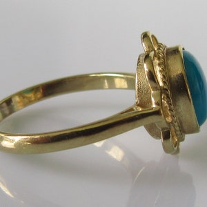 May include: A gold ring with a teal oval gemstone set in a rope-like design.