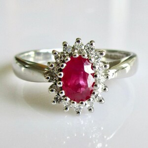 May include: A silver ring featuring a large oval ruby set within a halo of smaller diamonds.