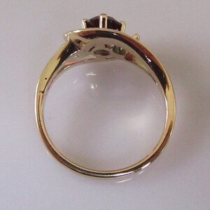 May include: A gold ring with a red gemstone and two smaller gemstones. The ring is set in a twisted band.