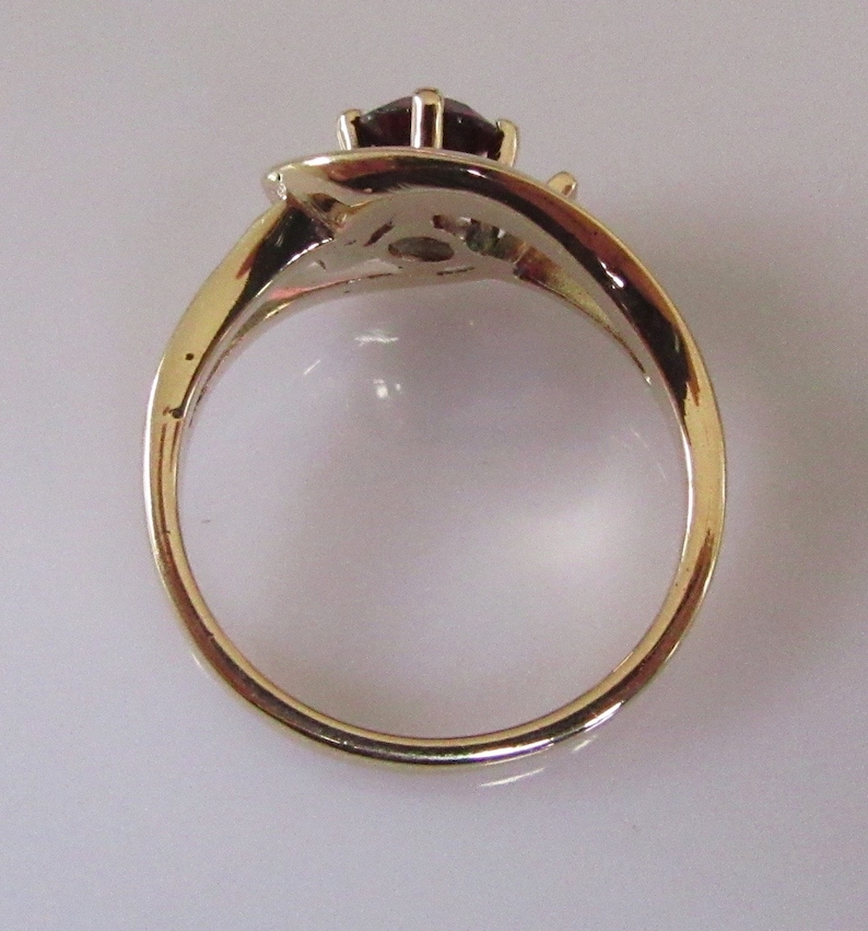 May include: A gold ring with a red gemstone and two smaller gemstones. The ring is set in a twisted band.