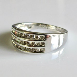 May include: A silver band ring with three rows of small, clear diamonds.