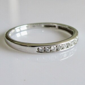 May include: A thin silver band with a row of small diamonds set in a channel setting.