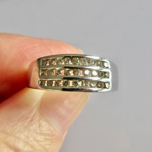 May include: A silver band ring with three rows of small, clear diamonds.
