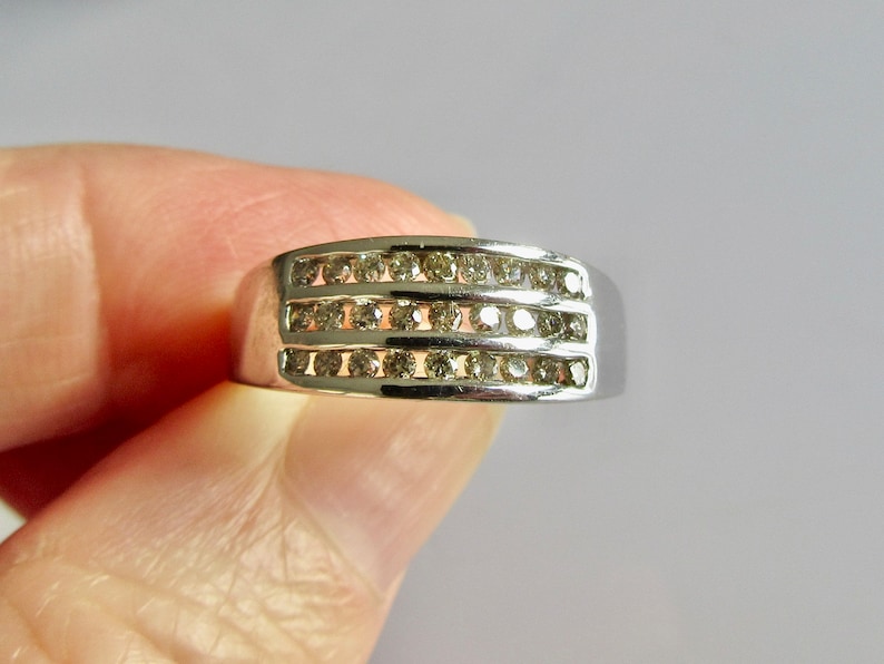 May include: A silver band ring with three rows of small, clear diamonds.