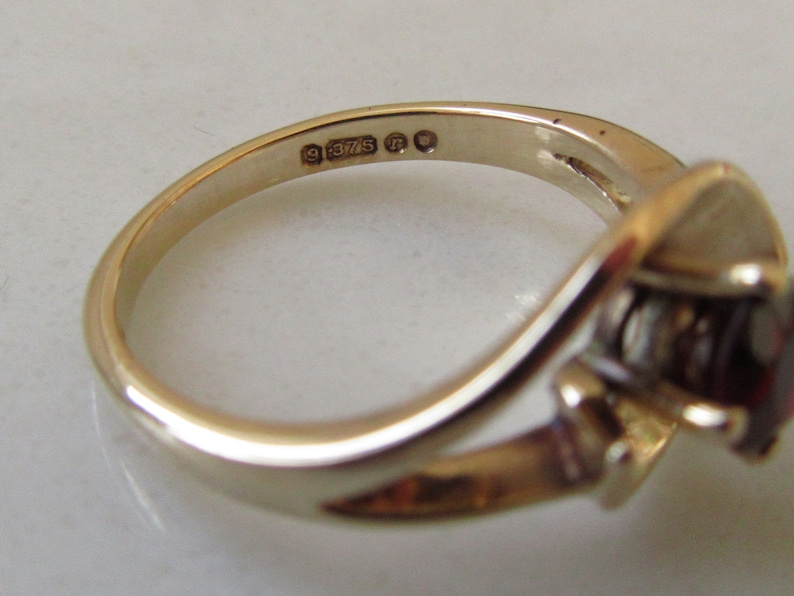 May include: A gold ring with a red gemstone and a smaller diamond accent. The inside of the band is stamped with "9 375" and a hallmark.