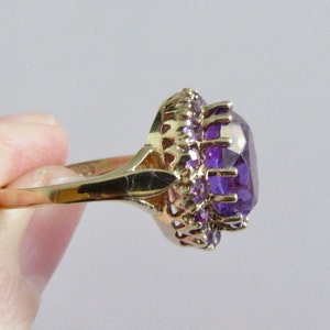 May include: A gold ring with a large, faceted amethyst gemstone surrounded by smaller amethyst stones.