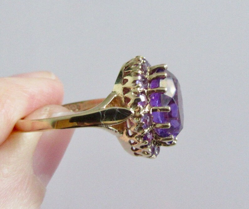 May include: A gold ring with a large, faceted amethyst gemstone surrounded by smaller amethyst stones.