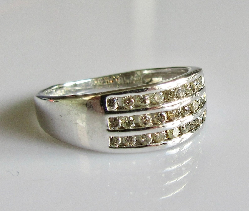 May include: A silver band ring with three rows of small, clear diamonds.