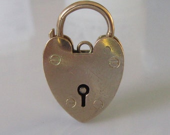 Può includere: Un ciondolo a forma di cuore con lucchetto dorato, con un buco della serratura e dettagli decorativi.
