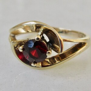 May include: A gold ring with a red gemstone set in a swirl design.