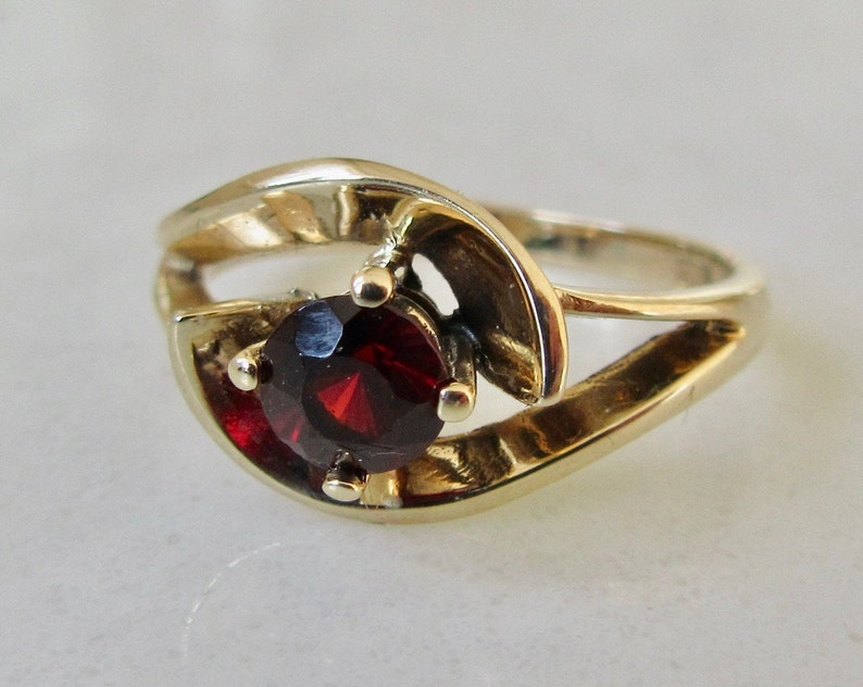 May include: A gold ring with a red gemstone set in a swirl design.