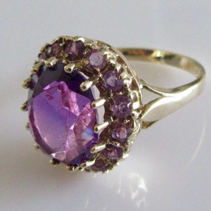 May include: A gold ring with a large, faceted purple gemstone surrounded by a halo of smaller purple gemstones.