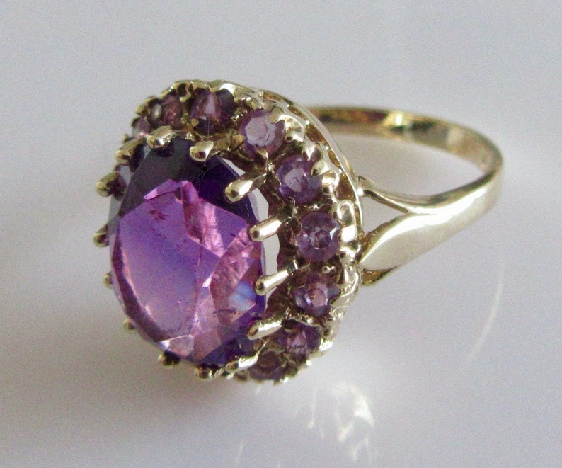 May include: A gold ring with a large, faceted purple gemstone surrounded by a halo of smaller purple gemstones.