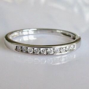 May include: A thin silver band with a row of small, clear diamonds set in a channel setting.
