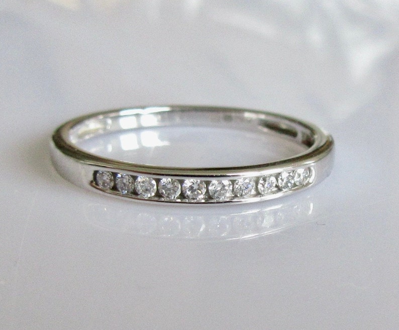 May include: A thin silver band with a row of small, clear diamonds set in a channel setting.