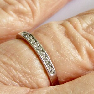 May include: A thin silver band with a row of small, clear diamonds set in a channel setting.