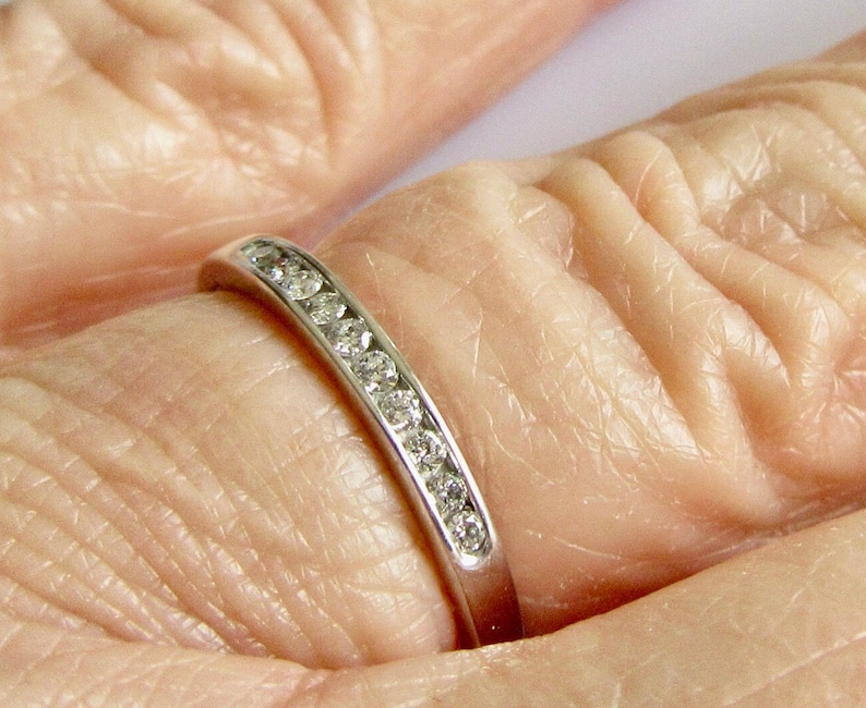 May include: A thin silver band with a row of small, clear diamonds set in a channel setting.