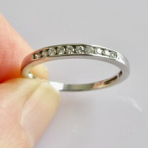 May include: A thin silver band with a row of small diamonds set in a channel setting.