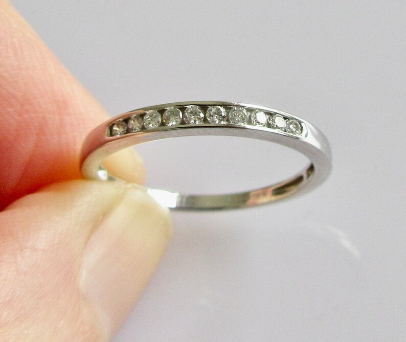 May include: A thin silver band with a row of small diamonds set in a channel setting.