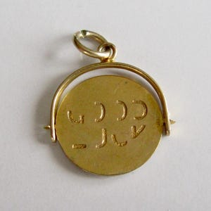 Peut inclure: Un pendentif circulaire de couleur dorée doté d'un disque central rotatif maintenu dans un cadre métallique incurvé. La surface plate du disque est gaufrée avec une série de petites marques incurvées et linéaires disposées sur deux rangées.