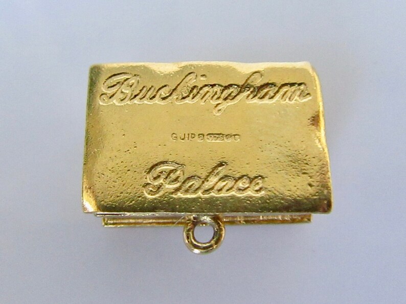 Puede incluir: Encanto de color dorado con forma de libro con las palabras "Buckingham Palace" grabadas en la parte delantera. El encanto tiene un peque&ntilde;o bucle en la parte superior para sujetarlo a una pulsera o collar.