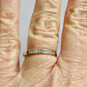 May include: A thin silver band with a row of small diamonds set in the metal.