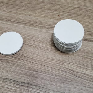 Pode incluir: Uma pilha de  copos de papel redondos brancos sobre uma superf&iacute;cie de madeira. H&aacute; um &uacute;nico copo &agrave; esquerda da pilha.