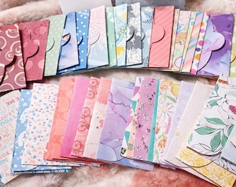 May include: A collection of small paper envelopes featuring a wide variety of colorful patterns, including floral prints, polka dots, geometric shapes, and abstract designs, arranged in overlapping rows with scalloped or rounded flap closures.