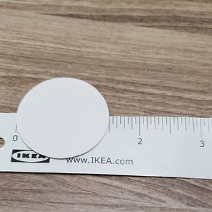 Pode incluir: Um c&iacute;rculo branco com aproximadamente 3,8 cm de di&acirc;metro, colocado em cima de uma r&eacute;gua branca com marcas pretas. A r&eacute;gua &eacute; etiquetada com "IKEA" e "www.IKEA.com".